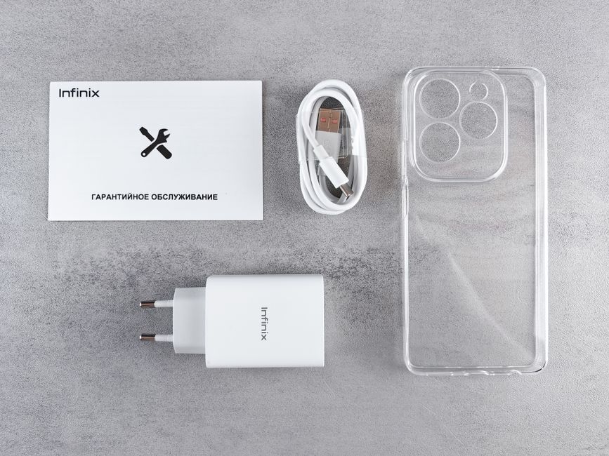 An organized flat lay of a smartphone case, white charge cable, transparent phone case, white charging adapter, and a small instruction manual with the Infinix logo and a black wrench icon, set agains